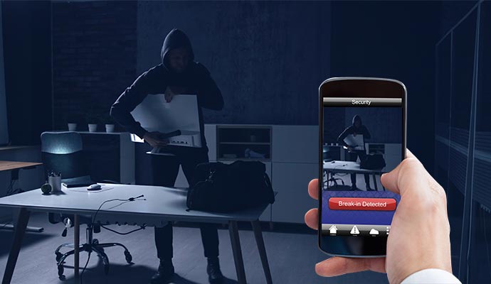 A person holding a smartphone displaying a security alert for a break-in